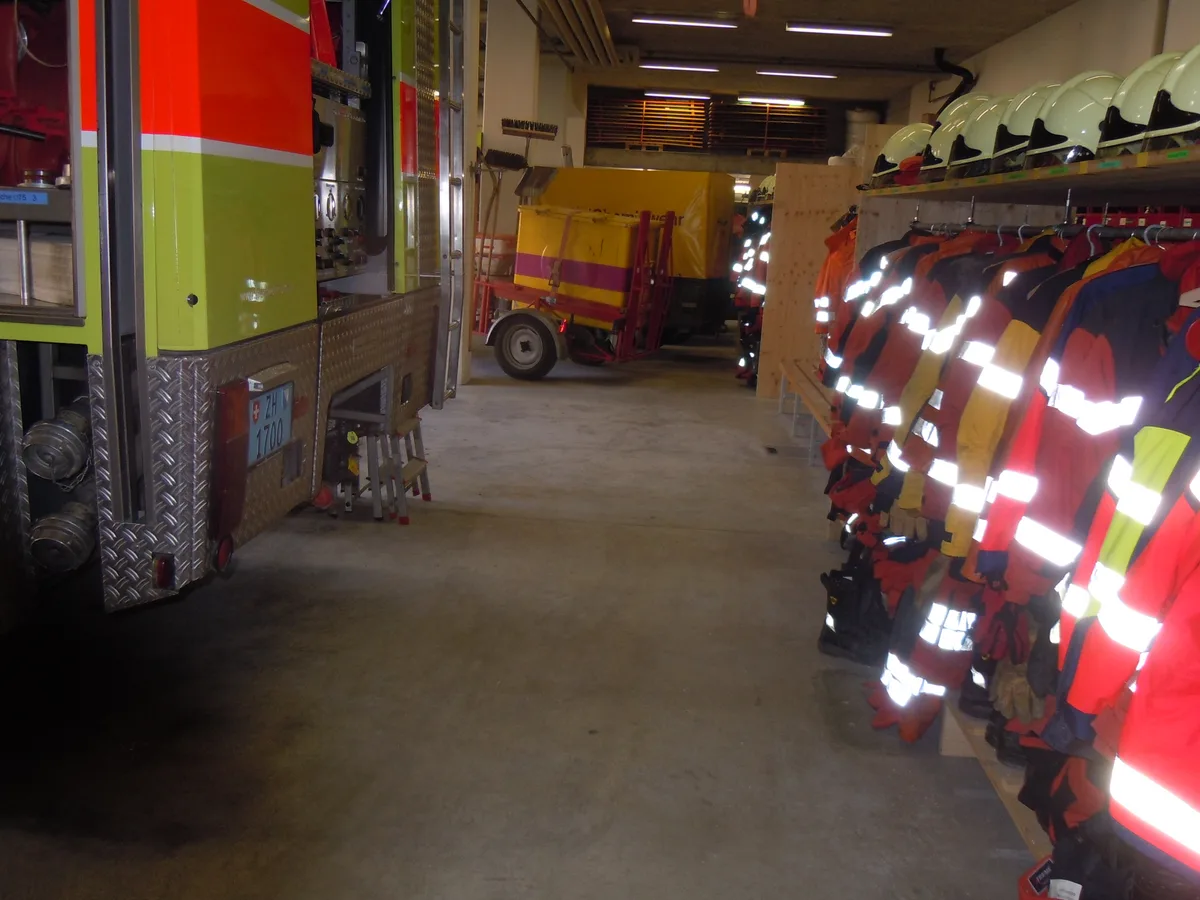 Halle mit Feuerwehrfahrzeugen und Jacken.